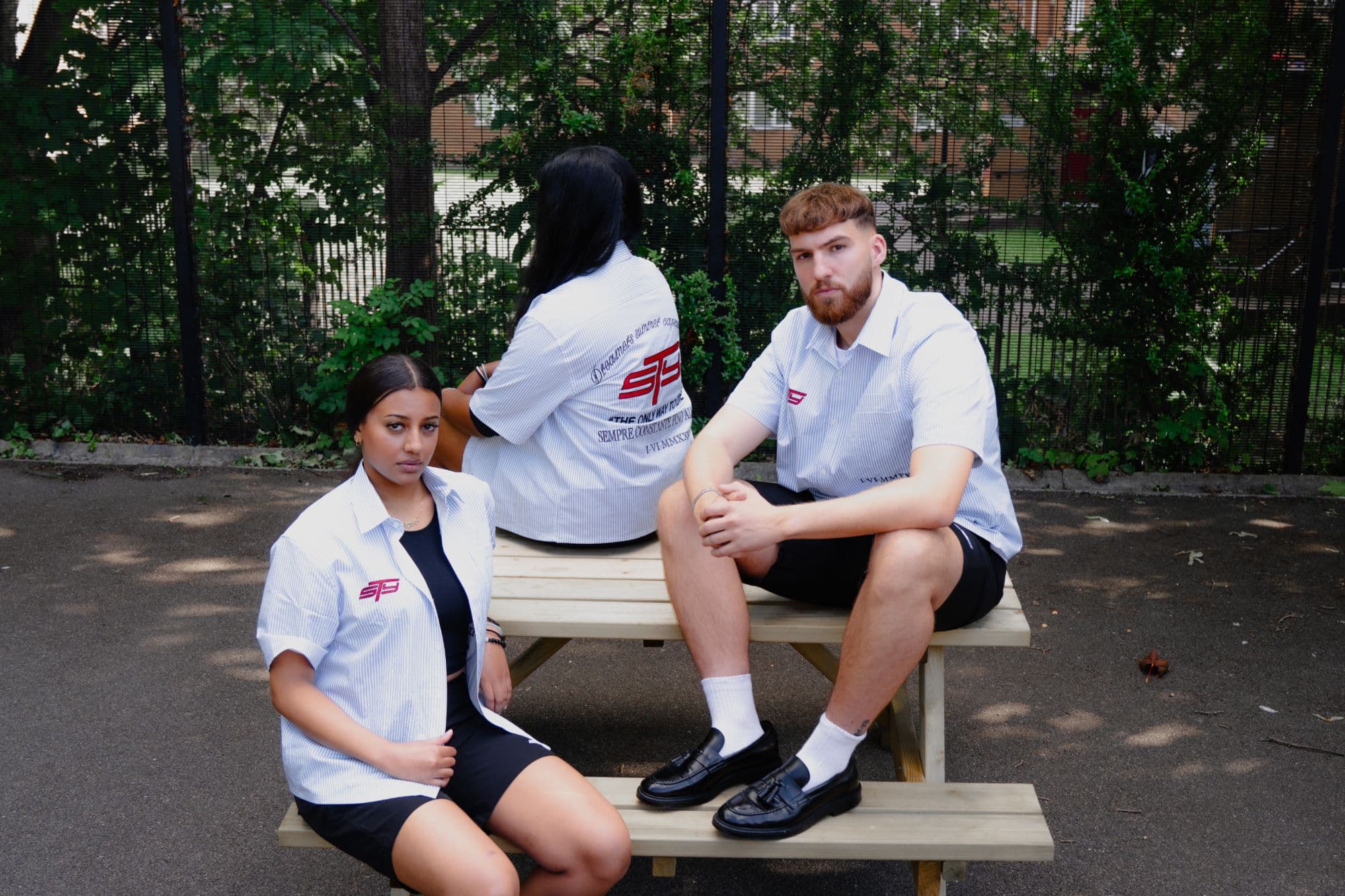 Steady campaign: three models in white pinstripe STY shirts with red embroidered logos, sitting on a picnic bench